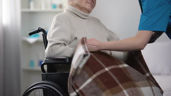 Nurse Covering Old Woman in Wheelchair With Blanket, Taking Care About Patient