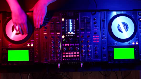 DJ turns vinyl records on turntable on mixing console in nightclub under neon lighting, closeup, top