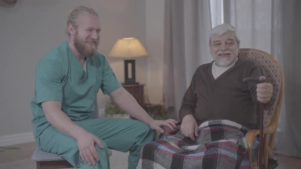 Portrait of Joyful Old Man Joking and Laughing Out Loud with Male Nurse Indoors