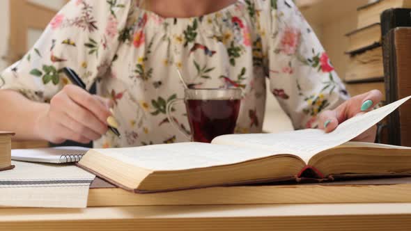 Student Female Reads Book and Writes Information in Notebook