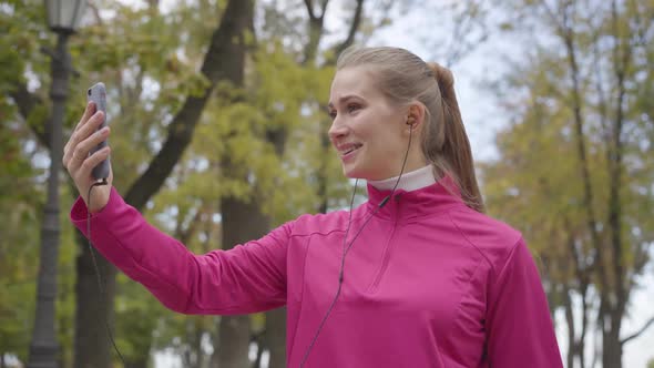 Portrait of Smiling Caucasian Sportswoman in Pink Sportswear Talking Through Videochat and Showing