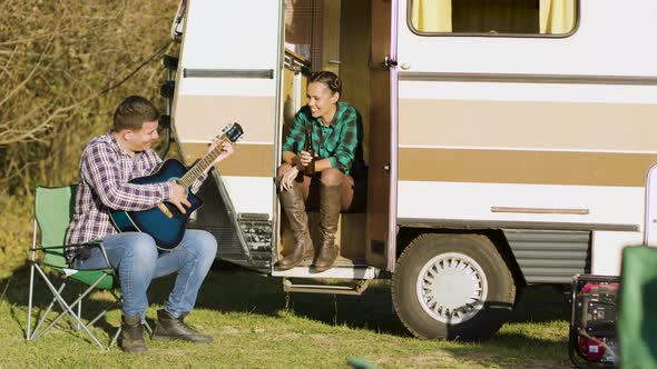 Boyfriend in Front of the Retro Camper Van Singing on Guitar