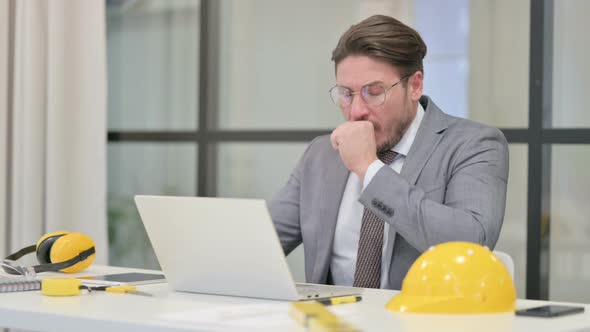 Middle Aged Engineer Coughing while using Laptop in Office