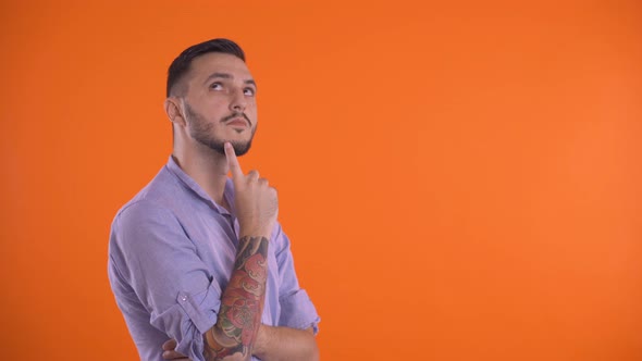 Thoughtful Man Thinking with Finger on Face, Isolated on Orange Background.