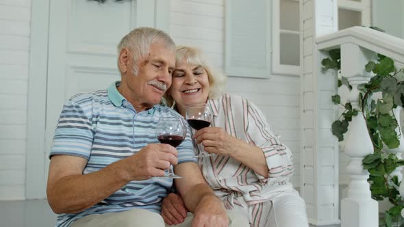 Attractive Senior Elderly Caucasian Couple Sitting and Drinking Wine in Porch at Home, Making a Kiss
