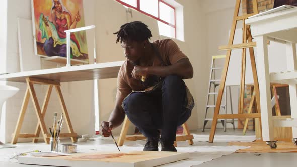 African american male artist wearing apron painting on canvas at art studio