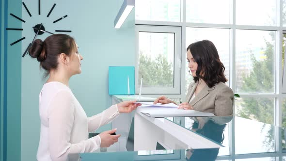 Woman Gives Forms to Fill to Client Near Counter in Hospital