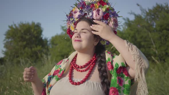 Portrait of Cute Plump Woman with a Wreath on Her Head Smiling in Sunlight on the Green Summer Field