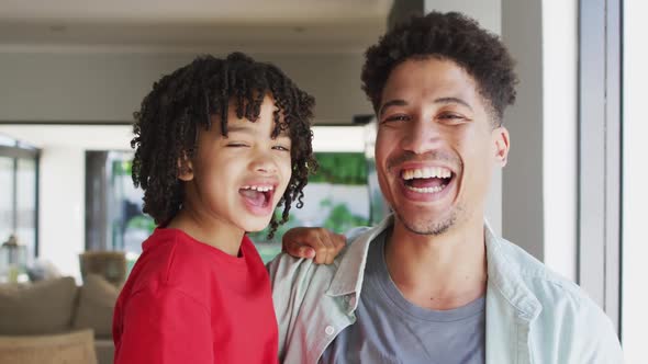 Portrait of happy biracial man and his son looking at camera and smiling