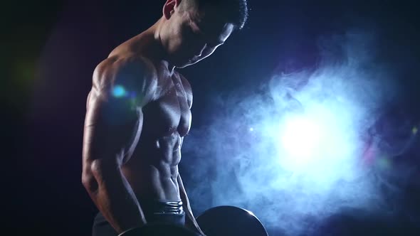 Asian Muscular Man Training Biceps with a Barbell, Black Smoke Background, Slow Motion