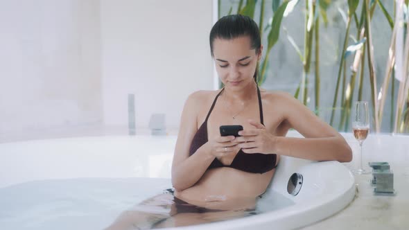 Young Woman Uses Smartphone Sitting in Modern Round Bathtub at Luxury Apartments