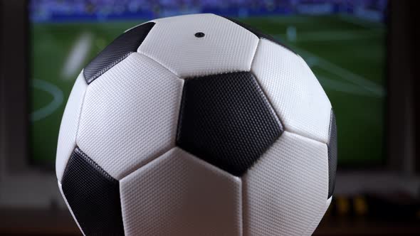A Black and White Soccer Ball on the Background of a TV with a Football Match
