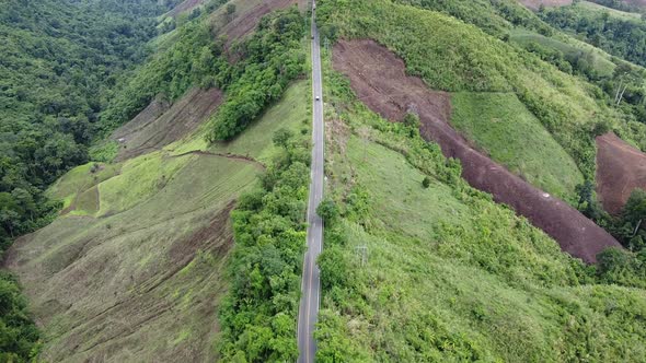 Aerial view of a car running along the mountain road through tropical forest in countryside by drone