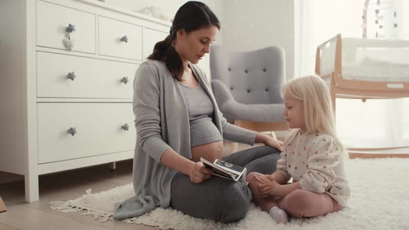 Caucasian woman in advanced pregnancy browsing ultrasound scan with her elementary daughter.