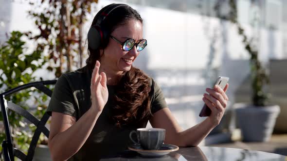 A Cheerful Woman in Funny Glasses Talks By Video Link While Sitting in an Outdoor Cafe
