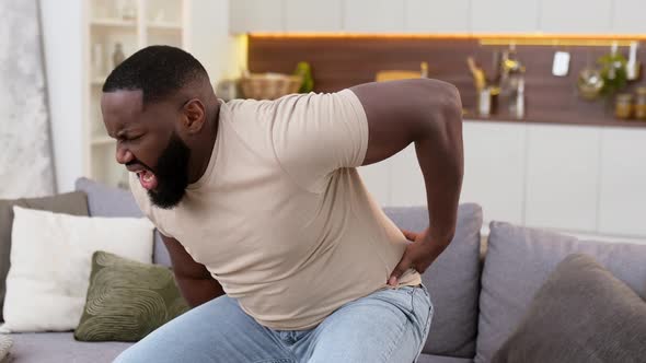 Sad Upset Young Adult African American Man in Casual Clothes Can't Get Up From the Couch in the