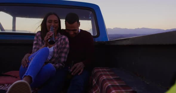 Young couple on a road trip sitting outside on their truck at dusk