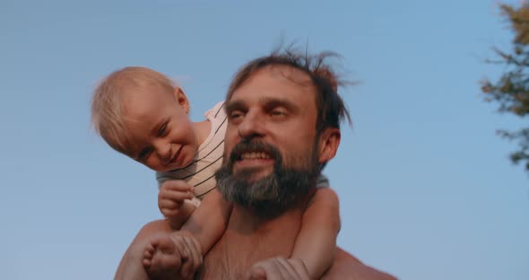 Happy Baby Son Sits on Father Neck and Have Fun Together Outdoor in Sunset