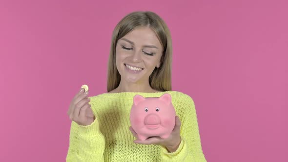 Ambitious Young Girl Inserting Coin in Piggy Bank Pink Background