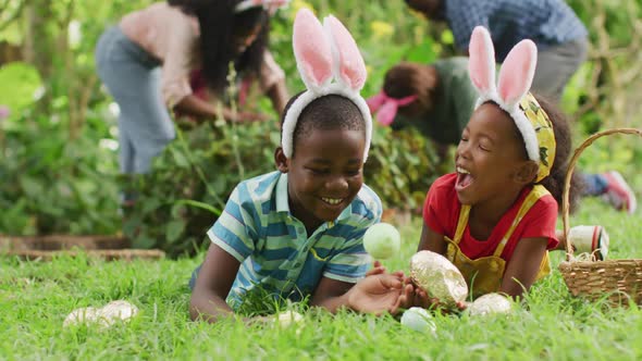 Animation of happy african american siblings lying on lawn with easter eggs