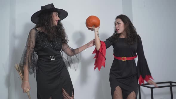 Two Colombian Girls In Witch Costumes Standing On Bed With One Holding A Broom And The Other Girl