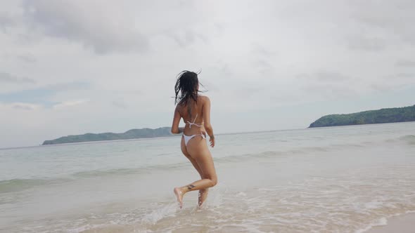 Young Woman In Bikini Running Along Beach