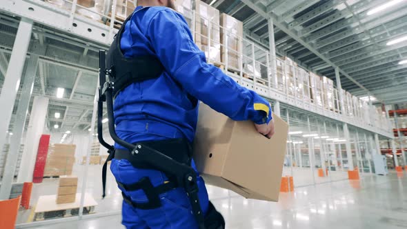 Storehouse Worker is Wearing Ergoskeleton and Carrying a Box