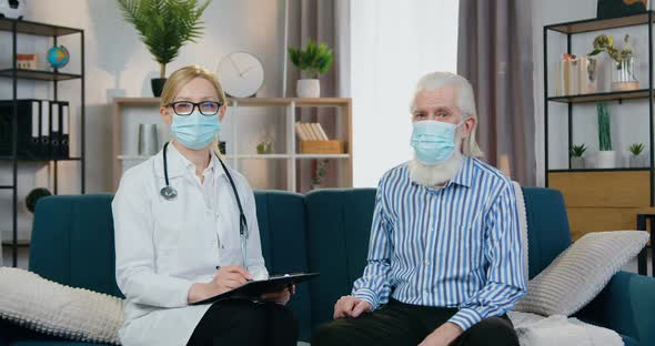 Doctor and Senior Man in Protective Masks Sitting in front of Camera During Doctor Home Visit
