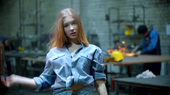 Young Sexy Woman in Checkered Shirt Standing in the Workshop and Playing with Her Hair - Man Working