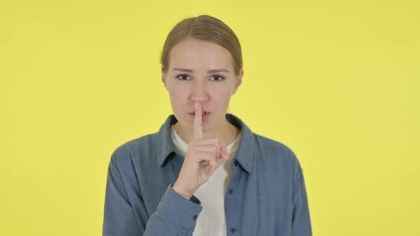 Young Woman with Finger on Lips Silence Yellow Screen