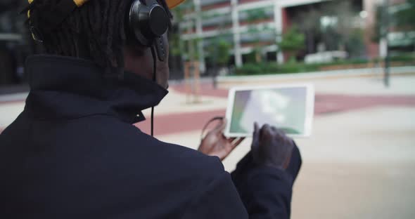 African American Man Works with Tablet Computer Urban Park Flips Through Feed on Social Networks