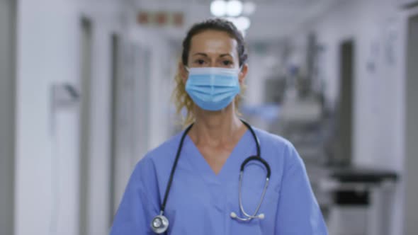 Portrait of caucasian female health worker wearing face mask in the corridor at hospital