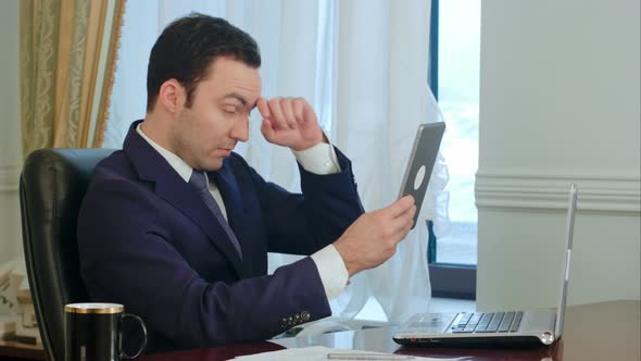 Elegant Businessman Correcting His Suit Jacket and Hair Looking at Modern Tablet