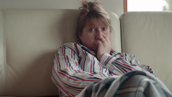 Emotional senior caucasian woman sits on the white sofa at home in front of the TV