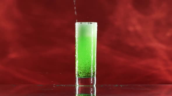 Brightgreen Soda Watter is Pouring Into Collins Glass Standing on Crimson Red Smoky Background in