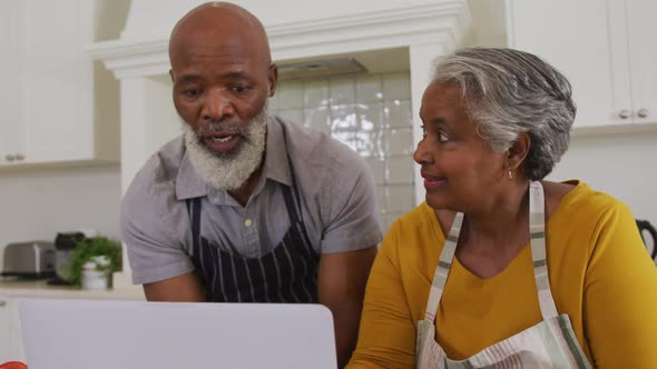 African american senior couple wearing aprons having a video call on laptop in the kitchen at home