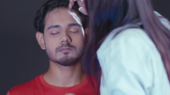 Make up artist applying white prosthetic insert on man's face to make a Halloween mask