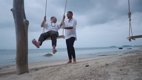 Married Happy Gay Couple Having Fun on a Beach Seaside Swing