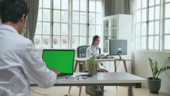 Asian Man Doctor Is Using Laptop Computer With Mock Up Green Screen Display In Workplace