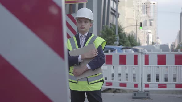 The Little Boy in Helmet, Hard Hat and Uniform Holding Building Plan, Controlling Work