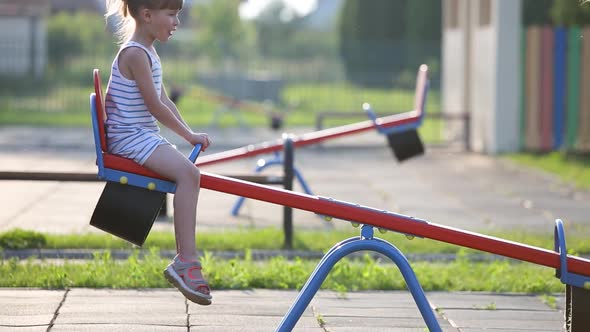 Cute Child Girl Playing Outside on a Seesaw Swing at Preschool Playground