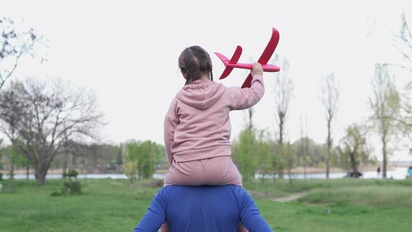 Happy family, dad, little daughter play together with a toy plane in the park.