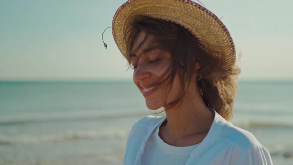 Smiling Young Woman in White Shirt and Straw Hat Standing on Background of Blue Sea and Sunset Sky