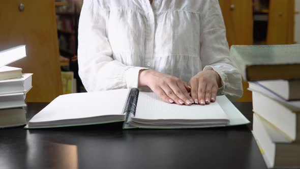 Female Student Studying in a Library Sitting and Reading a Braille Book