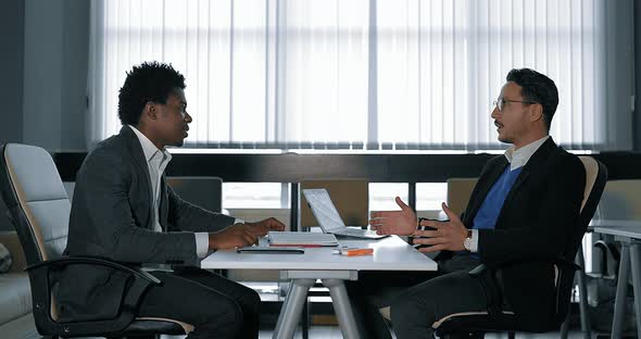 Two Young Businessman Talking at Desk in Office