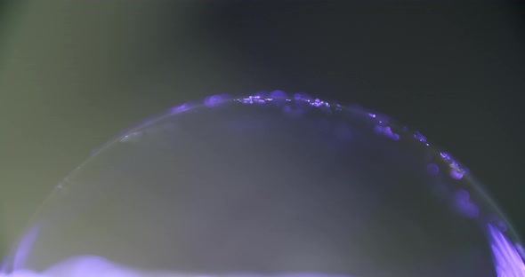 macro shot of a transparent sphere glowing purple in the dark. Little particlesing in the current of