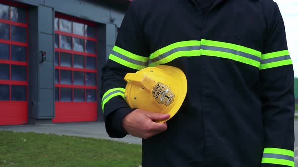 A Firefighter Stands in Front of a Fire Station with His Helmet on His Side - Closeup