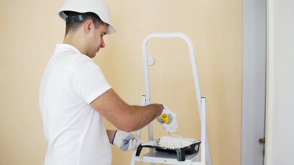 Painter Man in Helmet at Work with Roller Taking Color to Paint the Wall