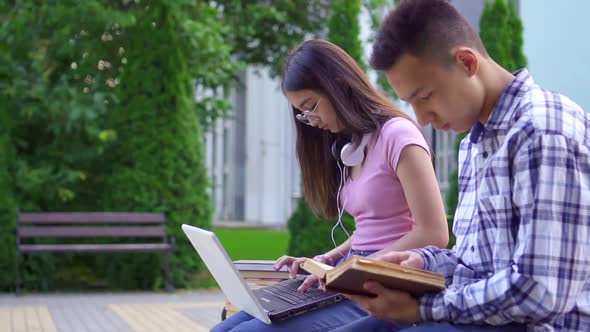 Young Male Asian Student with Book and Young Asian Woman with Laptop in Park Slow Mo