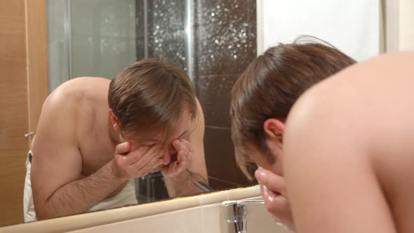 Man washing his face and looking at himself in the mirror.